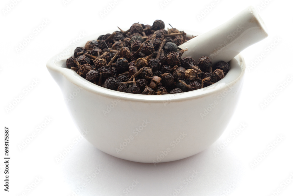 Close-up of Dry organic Sheetal Chini (Piper cubeba) seeds, in white ceramic mortar and pestle, isolated on a white background. Close-up of Dry organic Sheetal Chini (Piper cubeba) seeds, in white ceramic mortar and pestle, isolated on a white background.