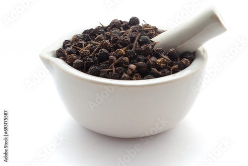 Close-up of Dry organic Sheetal Chini (Piper cubeba) seeds, in white ceramic mortar and pestle, isolated on a white background. photo