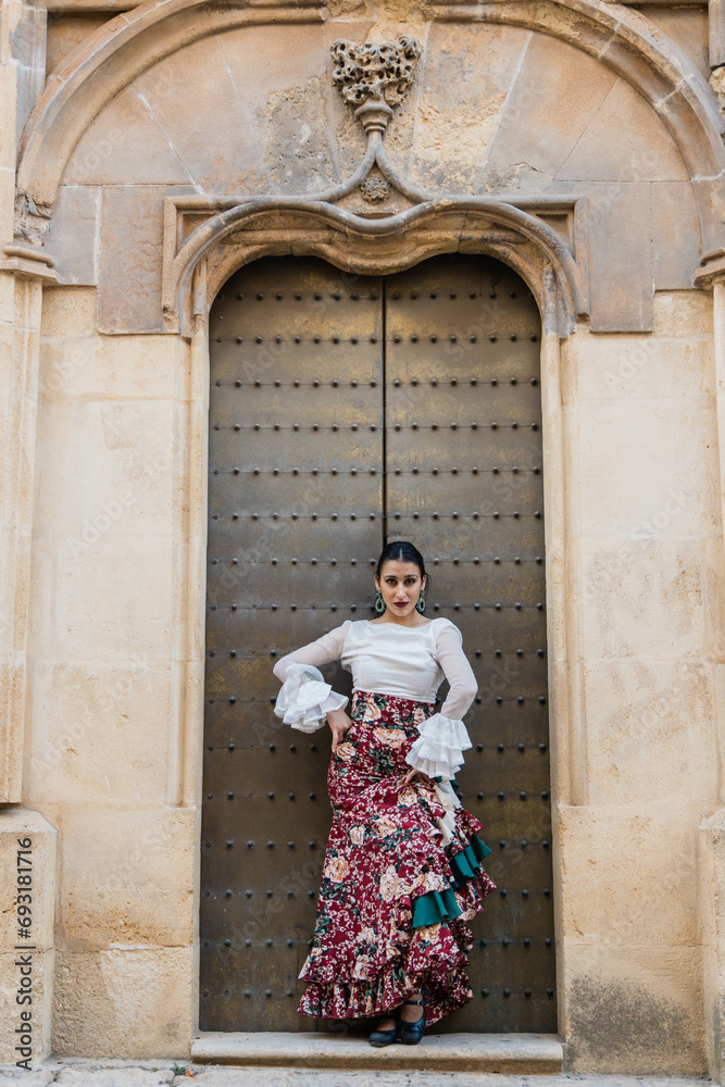 Gorgeous young ethnic woman in traditional dress standing near building door