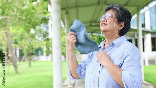 Elderly asian woman is fed up with the sweltering daytime heat making her uncomfortable, irritable and sweaty. She uses hat to cool herself down. photo