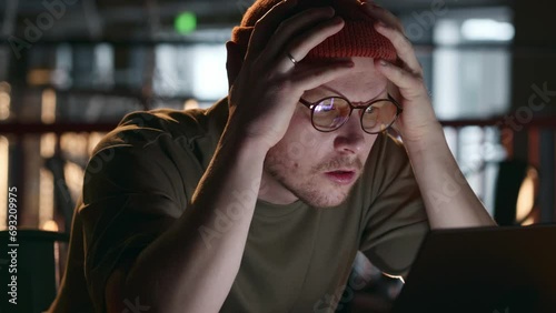 A programmer or hacker hipster millennial looks at the screen in frustration and surprise, holds his head and swears. The developer's reaction to errors in the program code. High quality 4k footage photo