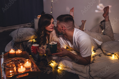 Romantic evening  cozy atmosphere  Christmas at home. Young attractive happy couple celebrating holidays  watching movies  drinking hot chocolate with marshmallow. Lazy weekend concept