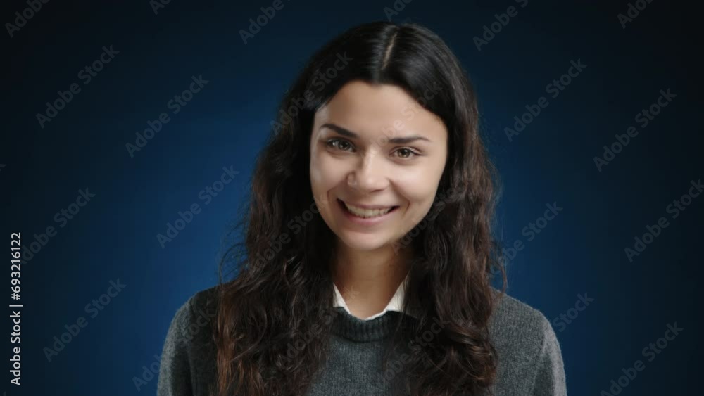 A happy girl winks one eye at the camera and smiles sincerely. She is standing against a dark blue background. High quality 4k footage A happy girl winks one eye at the camera and smiles sincerely. She is standing against a dark blue background. High quality 4k footage