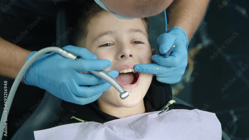Dental expert in medical gloves mask opening mouth of small patient with disposable napkin on chest, spraying water using dental turbine with water spray. High quality 4k footage Dental expert in medical gloves mask opening mouth of small patient with disposable napkin on chest, spraying water using dental turbine with water spray. High quality 4k footage