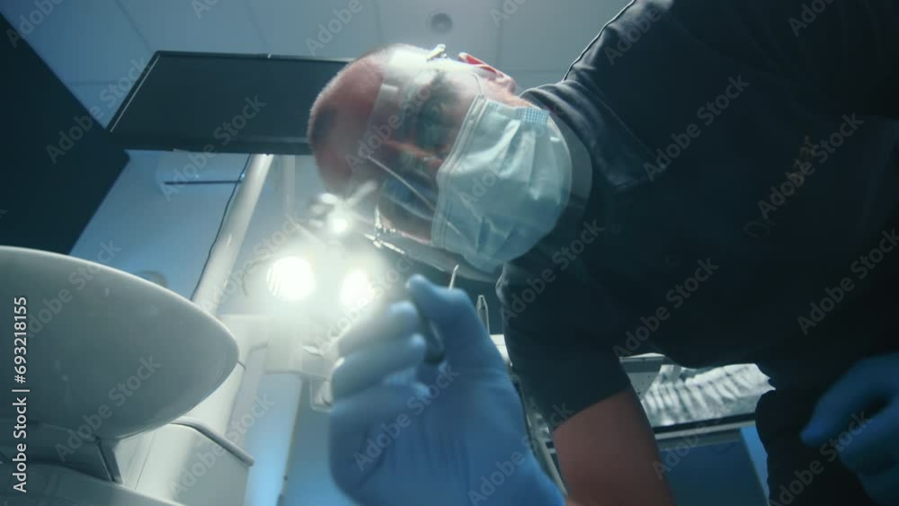 Male dentist in shield mask and latex gloves turning the light of dentist lamp on camera, spraying a stream of water from turbine, patient point of view. High quality 4k footage