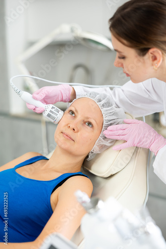 Fototapeta Naklejka Na Ścianę i Meble -  Young beautician with adult female client during hardware facial procedure in clinic. Concept of professional cosmetology and rejuvenation