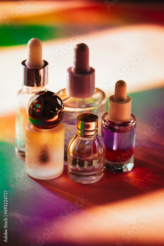 Set of small cosmetic pipette bottles on colorful rainbow shadows. Face, body oil products. Moisturizer facial cosmetic on a table. Beauty, beautician
