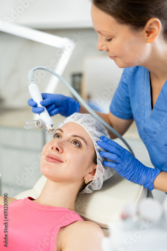 Beautiful female doctor making facial gas-liquid oxygen water epidermal peeling using professional equipment use macromolecule atomizing pen for young girl at modern spa salon. Skin care concept photo