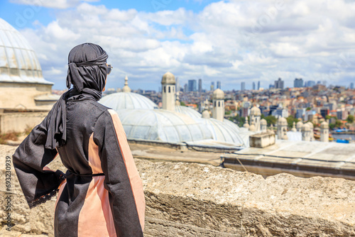 From Suleymaniye Mosque, Islamic woman in traditional Arab hijab dress takes in breathtaking panorama of Istanbul's skyline. Grand mosque, commissioned by Suleiman the Magnificent in 1500s in Turkey. photo