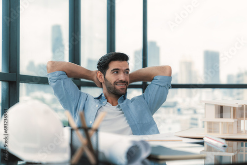 Portrait of relaxed young architect engineer resting and designing while sitting in modern home office. Male worker or manager take a break, holding hands behind head after finish project. Tracery