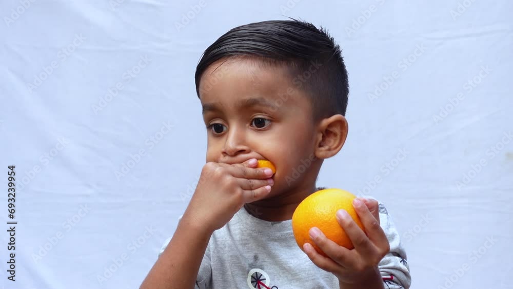 An Asian child is eating a slice of orange Citrus fruit on an isolated white background. A Kid holding or eating fresh Orange fruit. Fresh fruit-eating and enjoying concept 4k video. An Asian child is eating a slice of orange Citrus fruit on an isolated white background. A Kid holding or eating fresh Orange fruit. Fresh fruit-eating and enjoying concept 4k video.