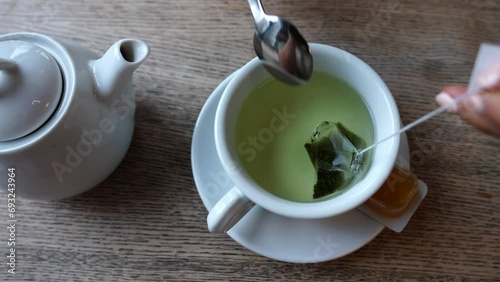 Girl manicure hand hold green tea bag in ceramic cup and stir in water photo
