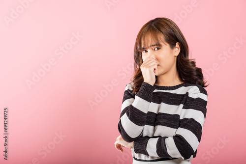 Portrait of a displeased Asian woman pinching her nose due to a bad smell. Studio shot isolated on pink background, highlighting healthcare. photo