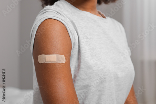 Young woman with adhesive bandage on her arm after vaccination indoors, closeup photo