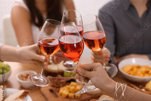 People clinking glasses with rose wine above wooden table indoors, closeup photo