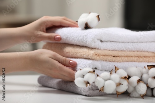 Woman taking terry towels and cotton flowers on white table indoors, closeup