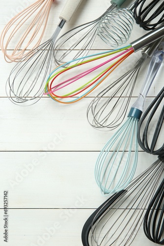 Different whisks on white wooden table, flat lay. Space for text