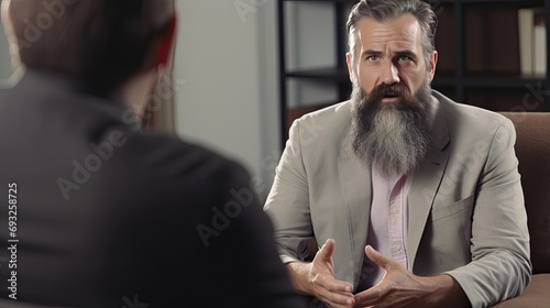 Middle aged bearded Caucasian man at an appointment with a psychologist. He delves into the problem and helps the patient solve it. The psychotherapist listens carefully to the patient’s story.