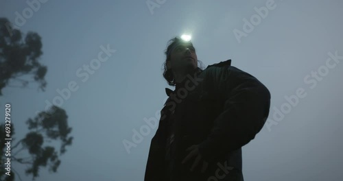 Flashlight, nature and man on an outdoor adventure or journey on a weekend trip or holiday. Freedom, camping and bottom view of young male person with head lamp at night for sightseeing in the woods. photo