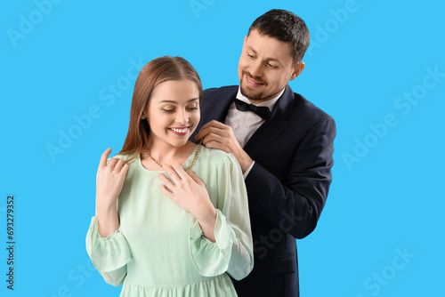 Young man putting necklace around his wife's neck on blue background