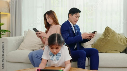 Family don't care about each other. Asian parents ignore their child and looking at their mobile phone at home, father and mother read social media but daughter play video game on sofa living room photo