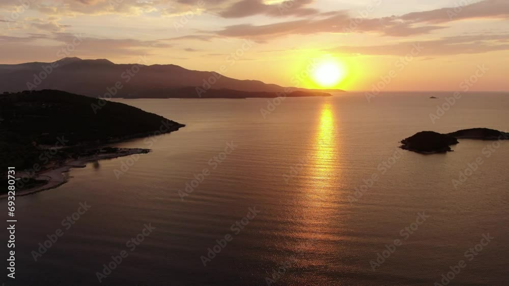 Drone view in Albania flying over blue crystal clear water on sunset, with the sun setting in the horizon with an island in Ksamil Drone view in Albania flying over blue crystal clear water on sunset, with the sun setting in the horizon with an island in Ksamil