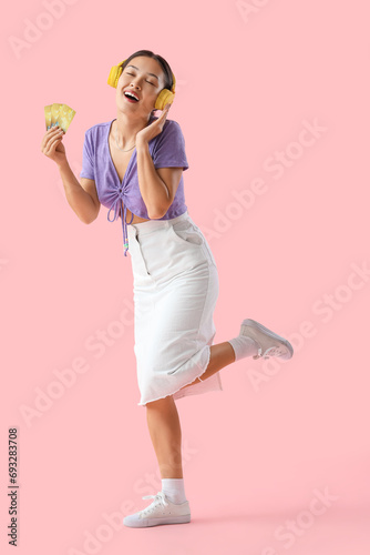 Young Asian woman in headphones with credit cards on pink background