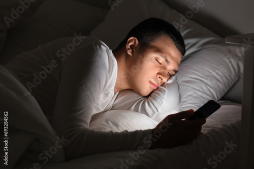 Young man with mobile phone sleeping in bed at night photo