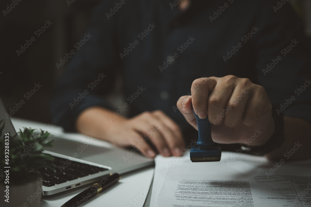 Man stamping approval on financial, banking, or investment documents at his desk official paperwork. rubber stamp with contract law and business documentation for legal agreements financial - obrazy, fototapety, plakaty 
