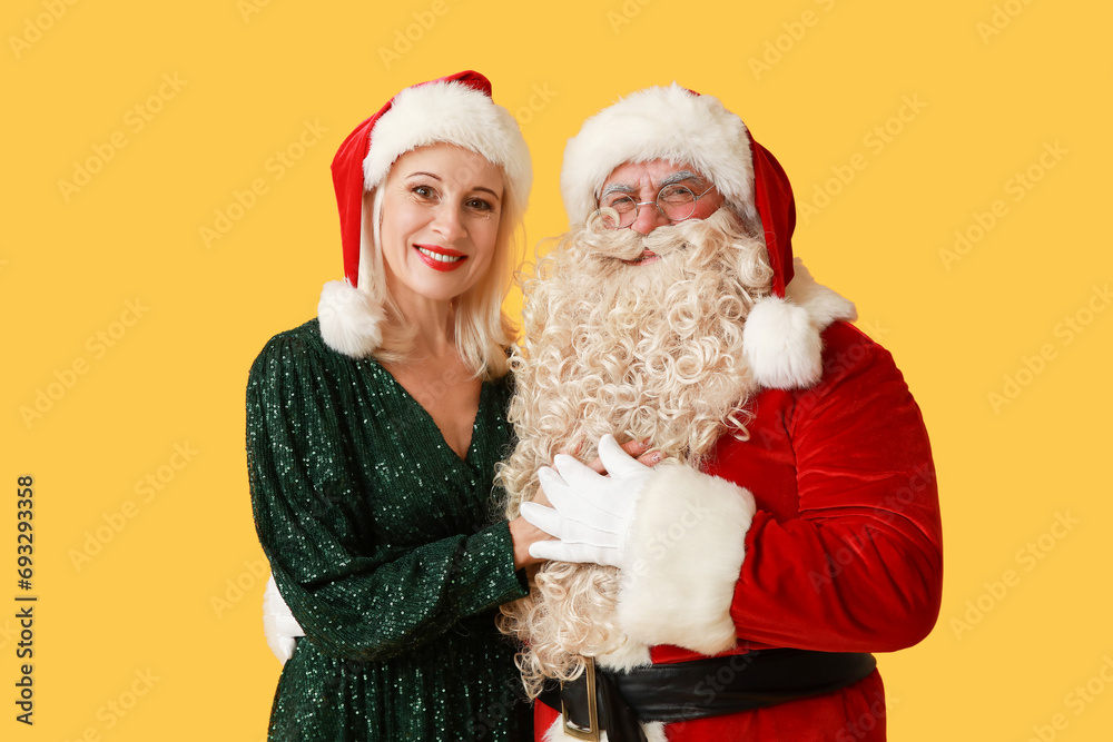 Santa Claus and beautiful mature woman in Christmas hats on yellow background Santa Claus and beautiful mature woman in Christmas hats on yellow background