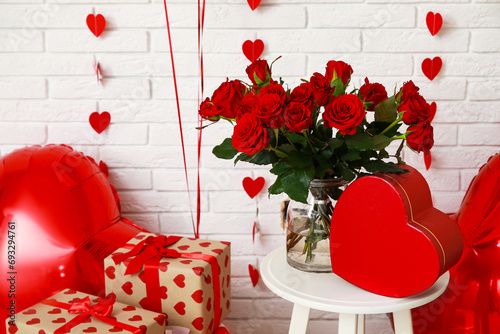 Air balloons with gift boxes and bouquet of red roses on white brick background. Valentine's day celebration