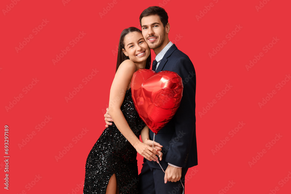 Beautiful young couple with heart shaped air balloon on red background. Valentine's day celebration Beautiful young couple with heart shaped air balloon on red background. Valentine's day celebration