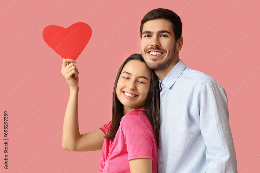 Beautiful young couple with red paper heart on pink background. Valentine's day celebration Beautiful young couple with red paper heart on pink background. Valentine's day celebration
