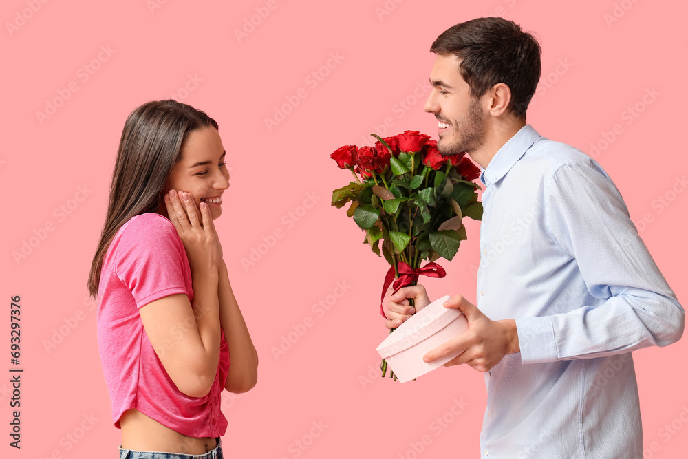 Beautiful young couple with bouquet of red roses and gift box on pink background. Valentine's day celebration Beautiful young couple with bouquet of red roses and gift box on pink background. Valentine's day celebration