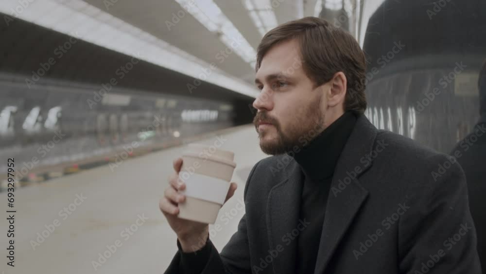 Medium shot of handsome young Caucasian man in black turtleneck and blazer drinking coffee from disposable cup while waiting for train at subway station Medium shot of handsome young Caucasian man in black turtleneck and blazer drinking coffee from disposable cup while waiting for train at subway station