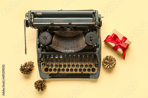 Vintage typewriter with Christmas gift and pine cones on yellow background
