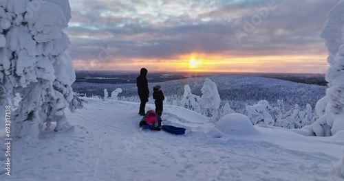 Aerial view low over mother and kids enjoying a cold, winter sunset in Lapland photo