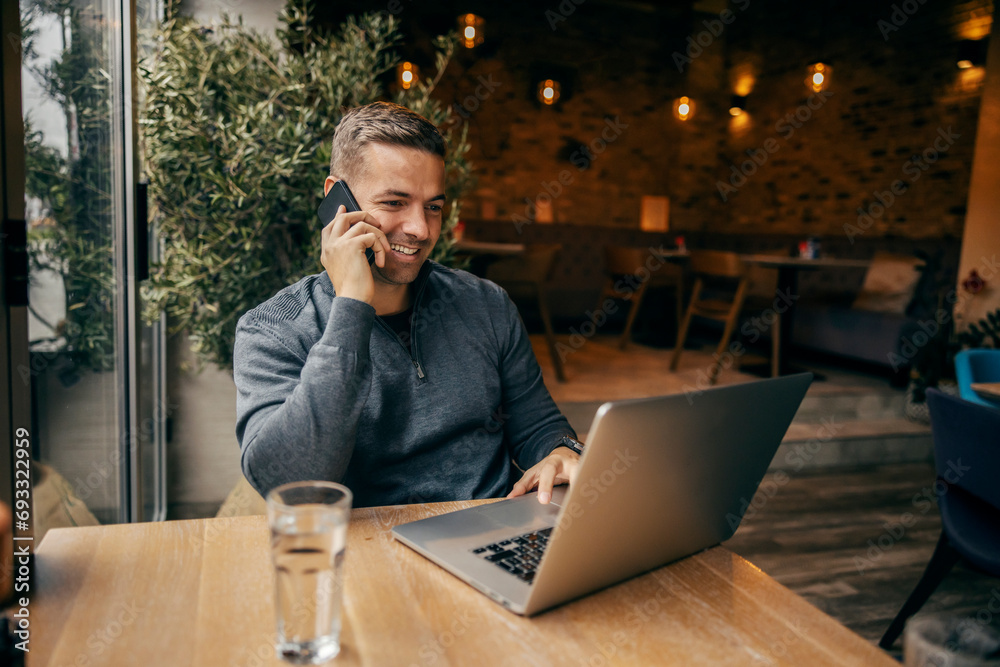 Portrait of a freelancer sitting in cafe, having a phone call and smiling at the laptop. Portrait of a freelancer sitting in cafe, having a phone call and smiling at the laptop.
