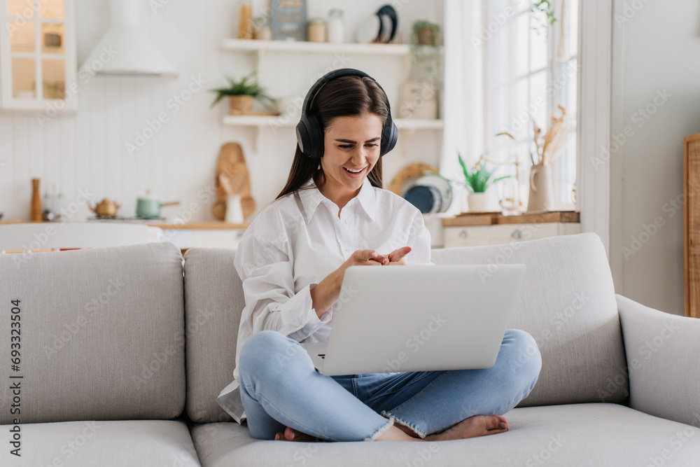 content young woman enjoys a relaxing moment, sitting cross-legged on a sofa with headphones and a laptop in a sunlit living space. content young woman enjoys a relaxing moment, sitting cross-legged on a sofa with headphones and a laptop in a sunlit living space.