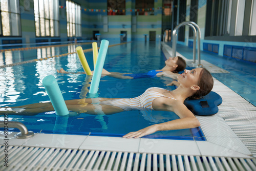 Two women doing relaxing exercise with noodles after training in swimming pool