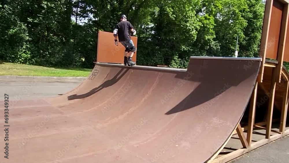 Ein Mann, der mit Inlineskates auf einer Halfpipe in einem Skatepark fährt. Der Mann trägt einen Helm und führt einen Trick aus. Die Rampe ist aus Holz und gebogen.