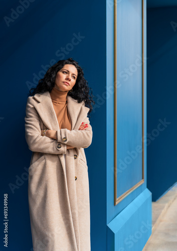 A woman in a coat against a wall, with a sad face
