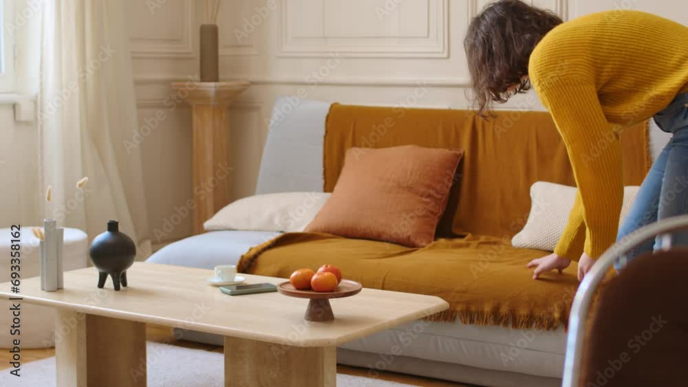 Brunette female adjusting blanket on couch in living room of luxury apartment Brunette female adjusting blanket on couch in living room of luxury apartment