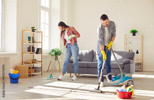 Young happy couple engages in home cleaning, with a vacuum and mop. They demonstrate togetherness and joyous teamwork, transforming household chores into moments of family connection. photo