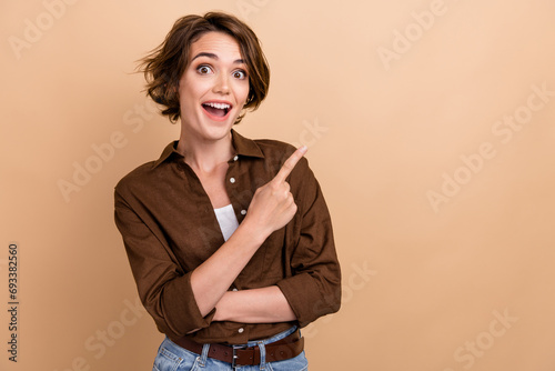 Photo of impressed funky lady wear brown shirt pointing finger empty space isolated beige color background