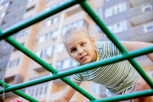 A young rock climber conquers an alpine staircase on a playground in a residential complex on a hot summer day. photo