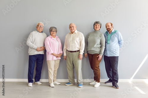 Group portrait of senior family members or friends. Several elderly people standing by wall. Retired old men and women in smart casual clothes standing together by grey wall. Older generation concept photo
