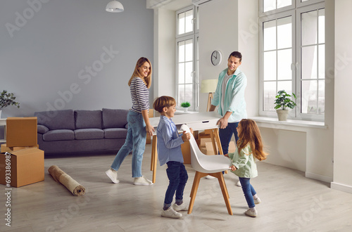 Happy family couple with two kids boy and girl arranging furniture table and chairs in a new apartment on moving day with unpacked boxes in background. Relocating, real estate, mortgage concept. photo