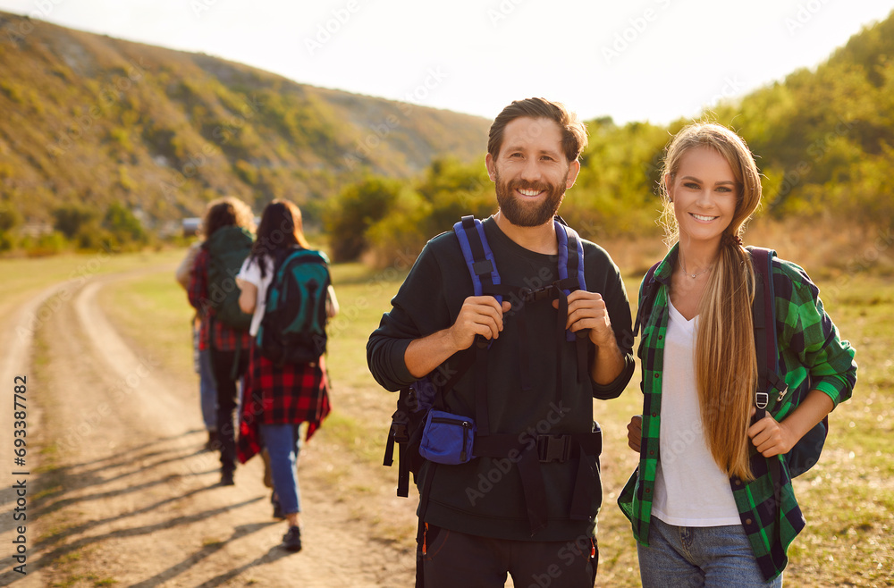 Portrait of a happy young smiling joyful friends tourists looking cheerful at the camera standing outdoor and having walking tour of the mountains. Hiking, adventure and people travel concept. Portrait of a happy young smiling joyful friends tourists looking cheerful at the camera standing outdoor and having walking tour of the mountains. Hiking, adventure and people travel concept.