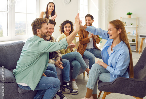 Portrait of a group of happy young friends students or coworkers giving high five reaching agreement sitting on sofa at home together. Young people men and women greeting each other. Teamwork concept photo